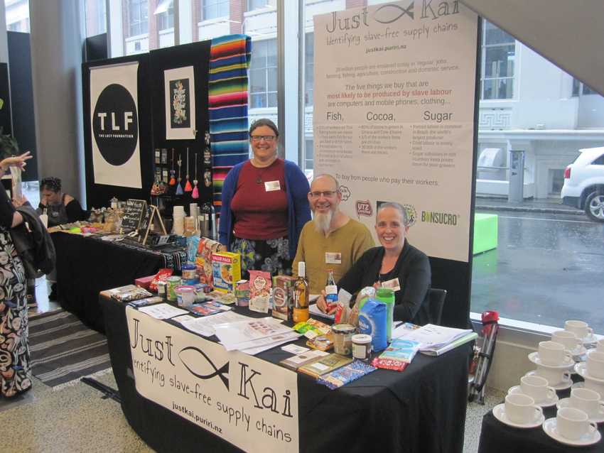 Heather, Martin and Anna behind the Just Kai table.  There are groceries on the table and a poster behind.