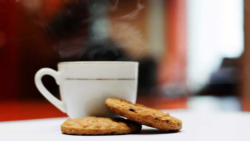 A steaming hot drink in a white cup with two biscuits on a table